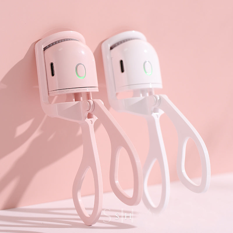 Popmarket electric heated eyelash curler in pink and white with ergonomic handles against a pink background