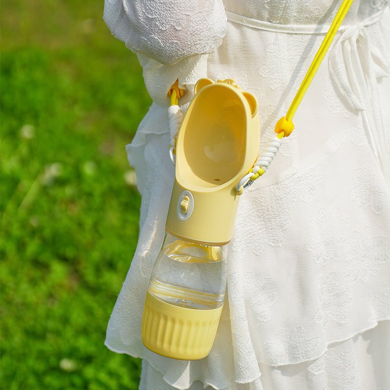 Yellow portable dog water bottle hanging on a person in white dress outdoors for small and big dogs