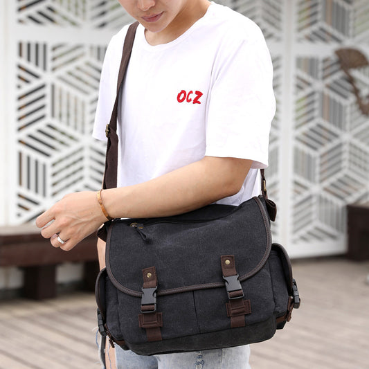 Person holding a black canvas bag with brown leather straps against a geometric-patterned wall.