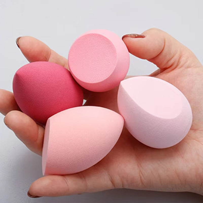 Hand holding four colorful makeup blender sponge cosmetic puffs in various shapes and shades of pink