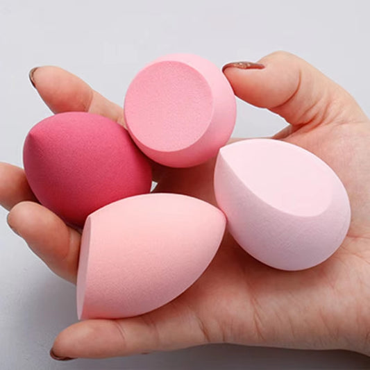 Hand holding four colorful makeup blender sponge cosmetic puffs in various shapes and shades of pink