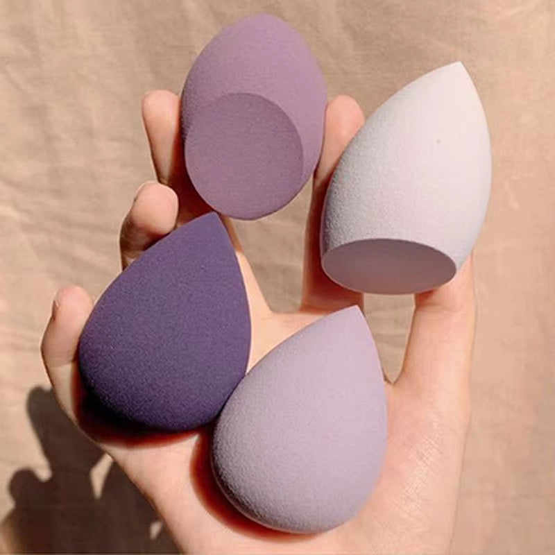 Hand holding four teardrop-shaped makeup blender sponge in various shades of purple and white