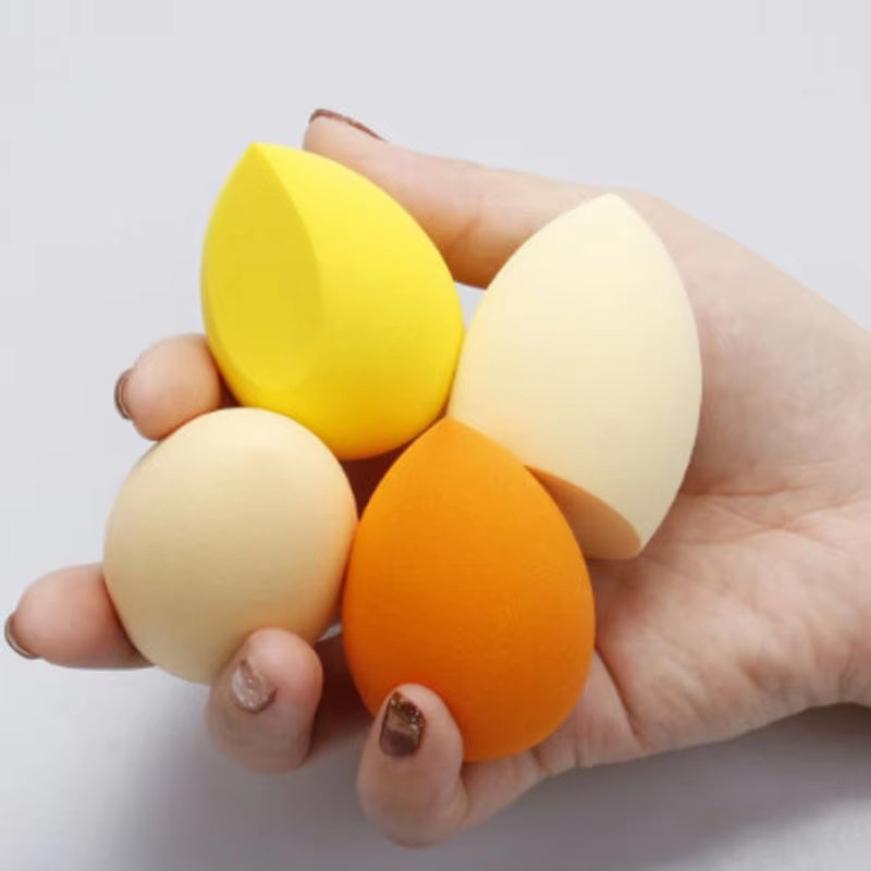 Hand holding four colorful makeup blender sponge cosmetic puffs in yellow, white, orange, and beige
