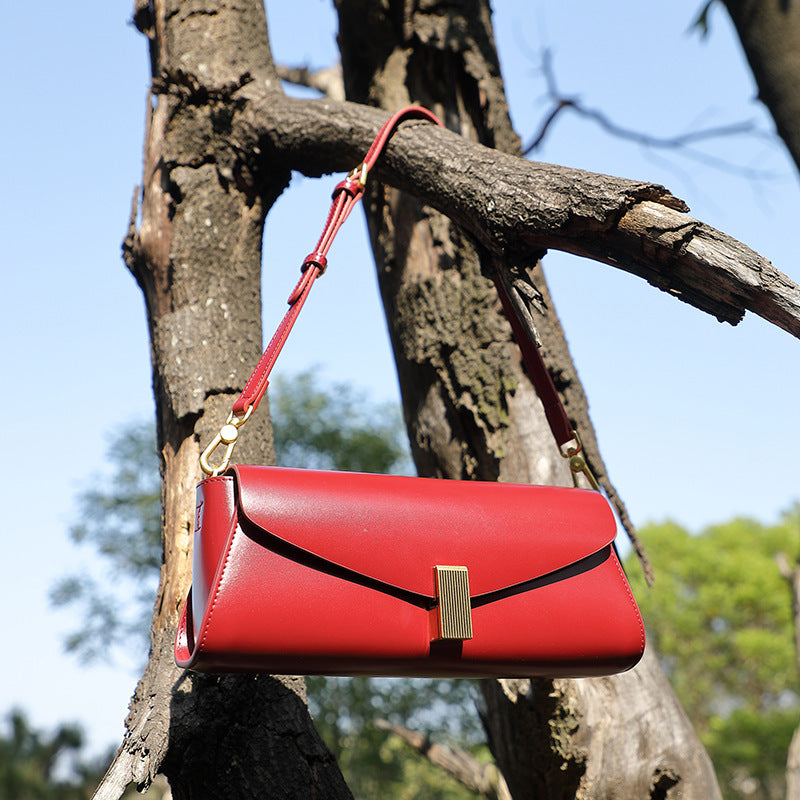 Red leather fashionable shoulder bag for women hanging on a tree branch outdoors