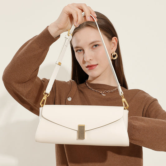Fashionable shoulder bag for women in white leather with gold hardware held by woman in brown sweater