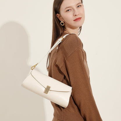 Fashionable shoulder bag for women white leather with gold clasp worn on shoulder by woman in brown sweater